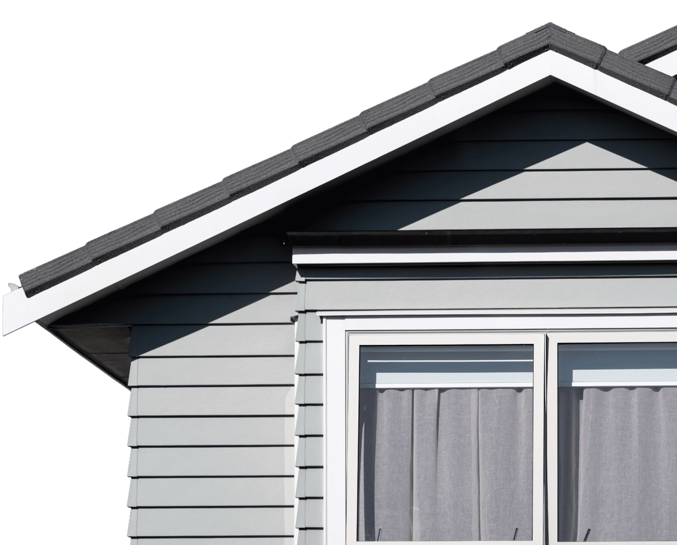 GettyImages-2004284554 1 A partial view of a gray house with a gable roof featuring black shingles. A window with closed curtains is visible below the roof.